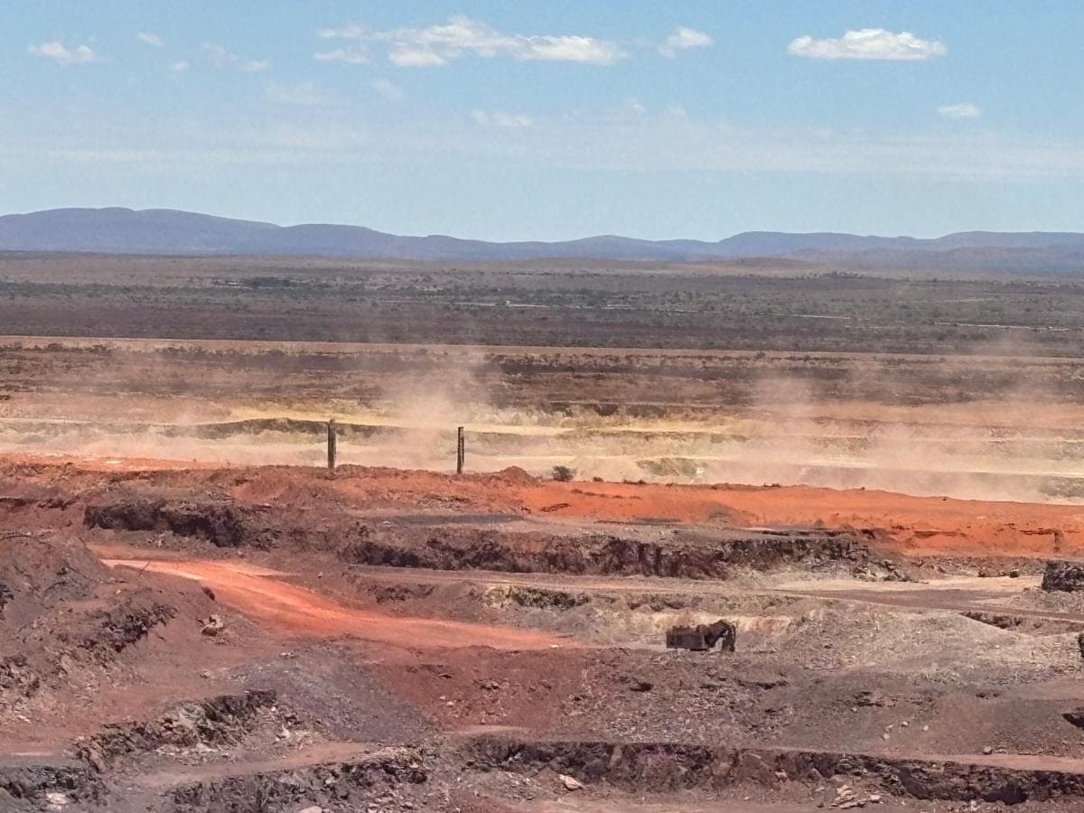 Open-pit workings running out to a distant escarpment, with dust drifting across the benches.