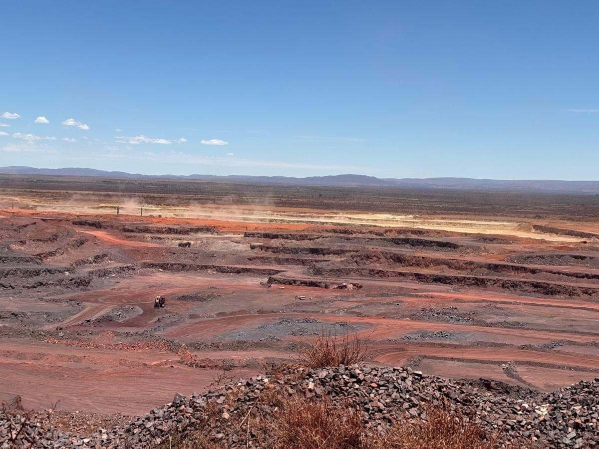 Wide view across a red open-pit mine, haul roads cut into the benches below the horizon.