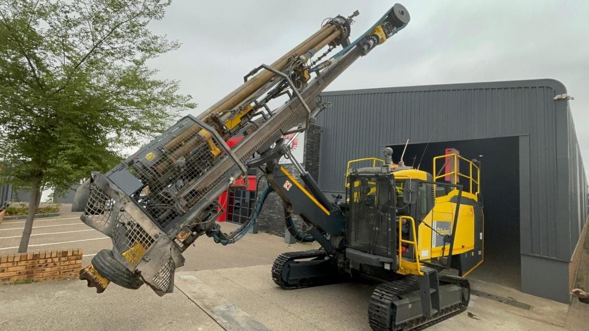 An Epiroc surface drill rig with its mast lowered, parked outside the Nsimbi workshop.