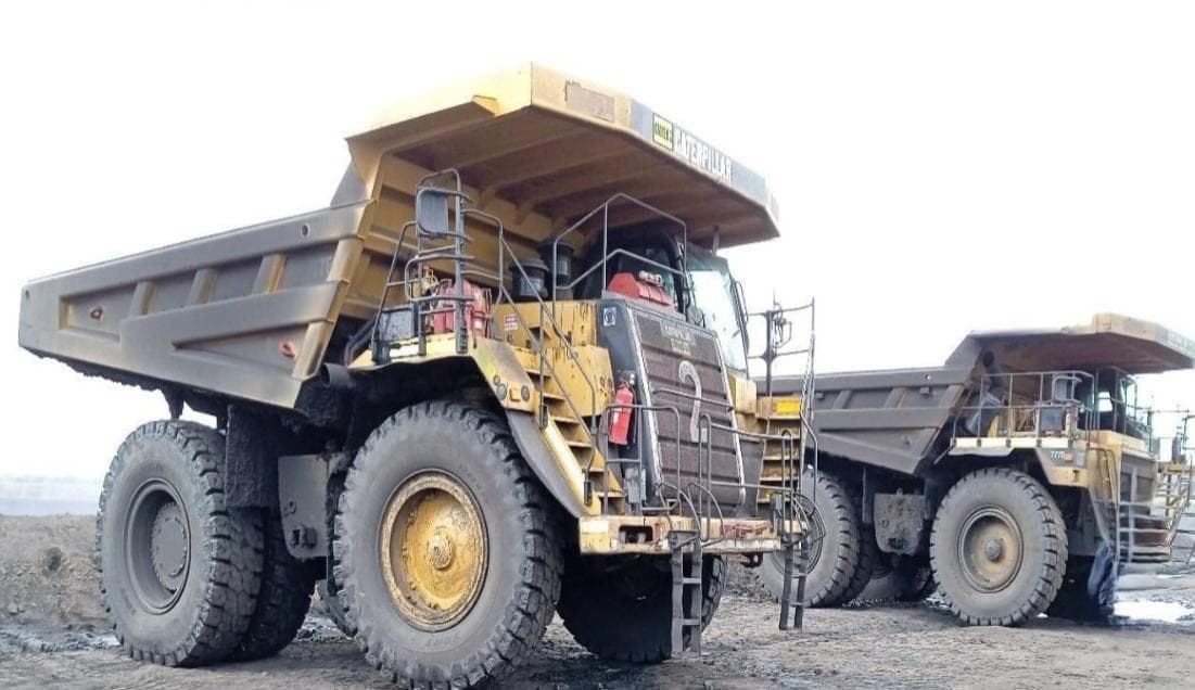 Two Caterpillar 777 haul trucks parked on the stockpile area.