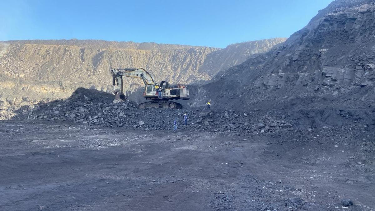 A tracked excavator loading at the toe of a coal face, with personnel standing off at a safe distance.
