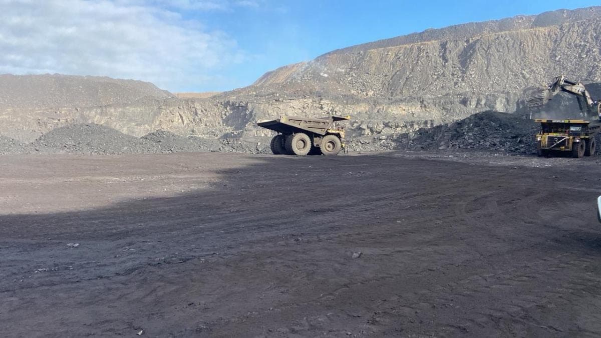 An empty haul truck turning on the pit floor, with an excavator working the face behind it.