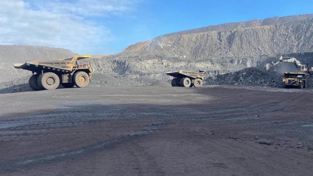 Three haul trucks queued on the pit floor beside an excavator loading from the coal face.