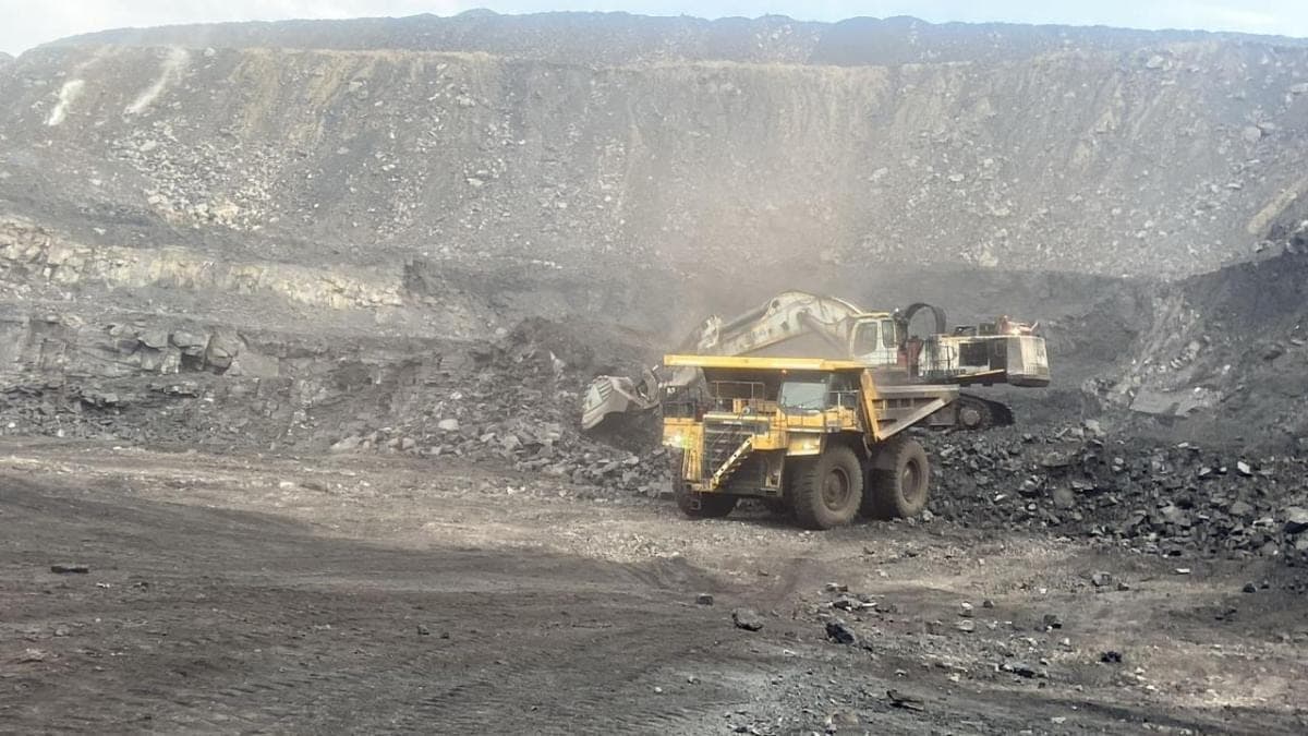 A haul truck spotted alongside an excavator at the face, with the high wall rising behind.