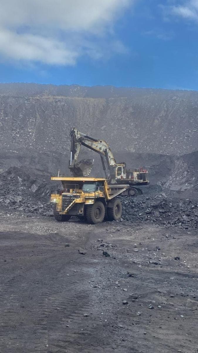 An excavator charging a haul truck at the coal face on a clear morning.