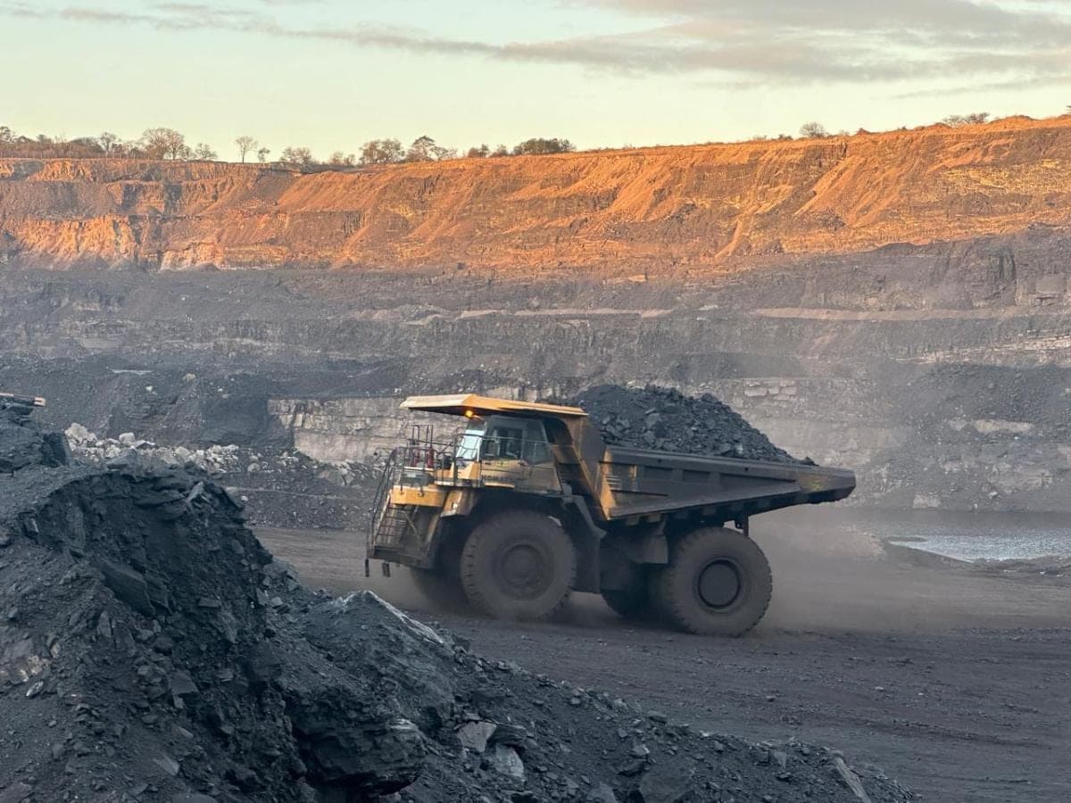 A loaded haul truck moving along the pit floor at sunrise, the high wall lit behind it.
