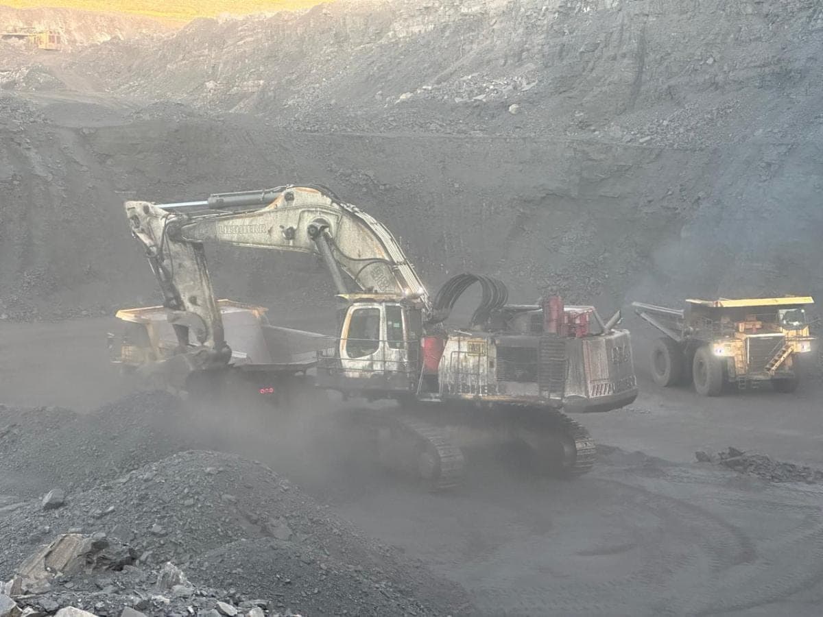 A Liebherr excavator working between two haul trucks in dense dust.