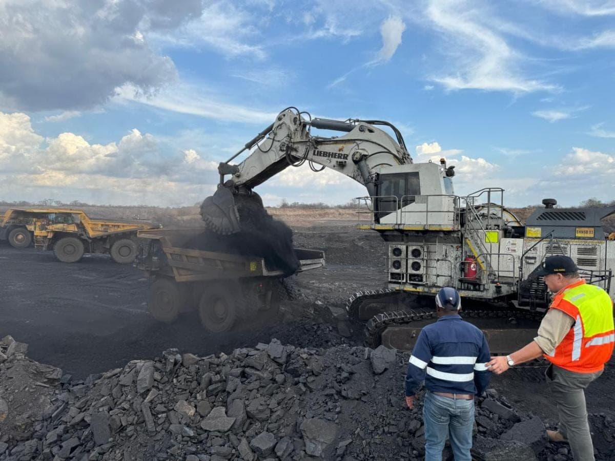 A Liebherr mining excavator loading a haul truck while two site personnel observe from the bench.