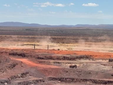 Open-pit workings running out to a distant escarpment, with dust drifting across the benches.