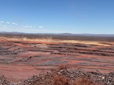 Wide view across a red open-pit mine, haul roads cut into the benches below the horizon.