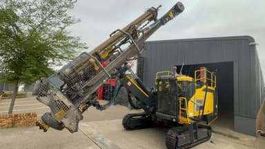 An Epiroc surface drill rig with its mast lowered, parked outside the Nsimbi workshop.