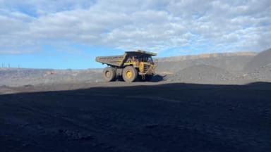 A Caterpillar haul truck crossing a coal bench under a broken sky.