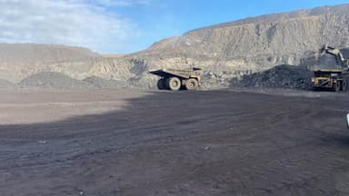 An empty haul truck turning on the pit floor, with an excavator working the face behind it.