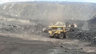 A haul truck spotted alongside an excavator at the face, with the high wall rising behind.