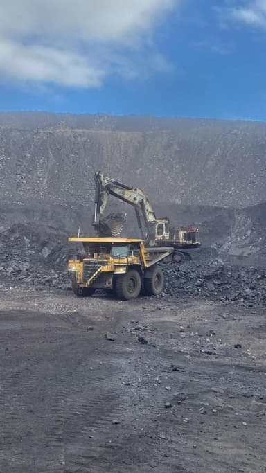 An excavator charging a haul truck at the coal face on a clear morning.