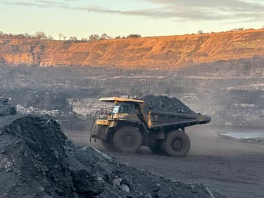 A loaded haul truck moving along the pit floor at sunrise, the high wall lit behind it.