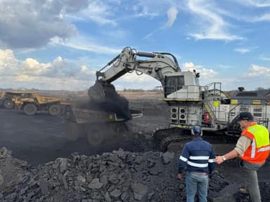 A Liebherr mining excavator loading a haul truck while two site personnel observe from the bench.